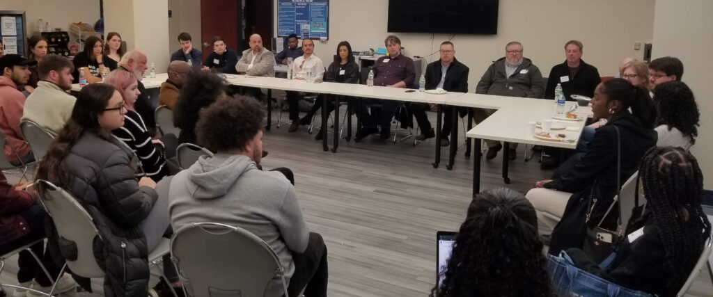 A large room with panelists at table and audience members looking on.