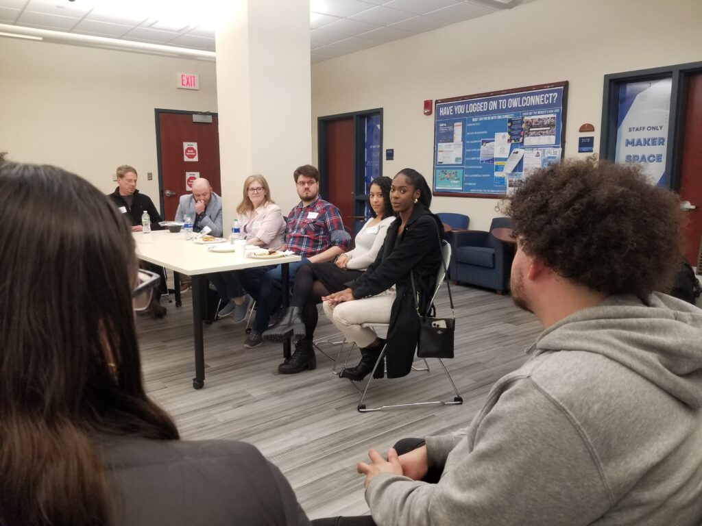 Panelists at a table look at students in an audience.